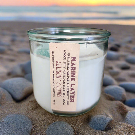 candle in recycled glass jar on a sunset beach with rock and sand