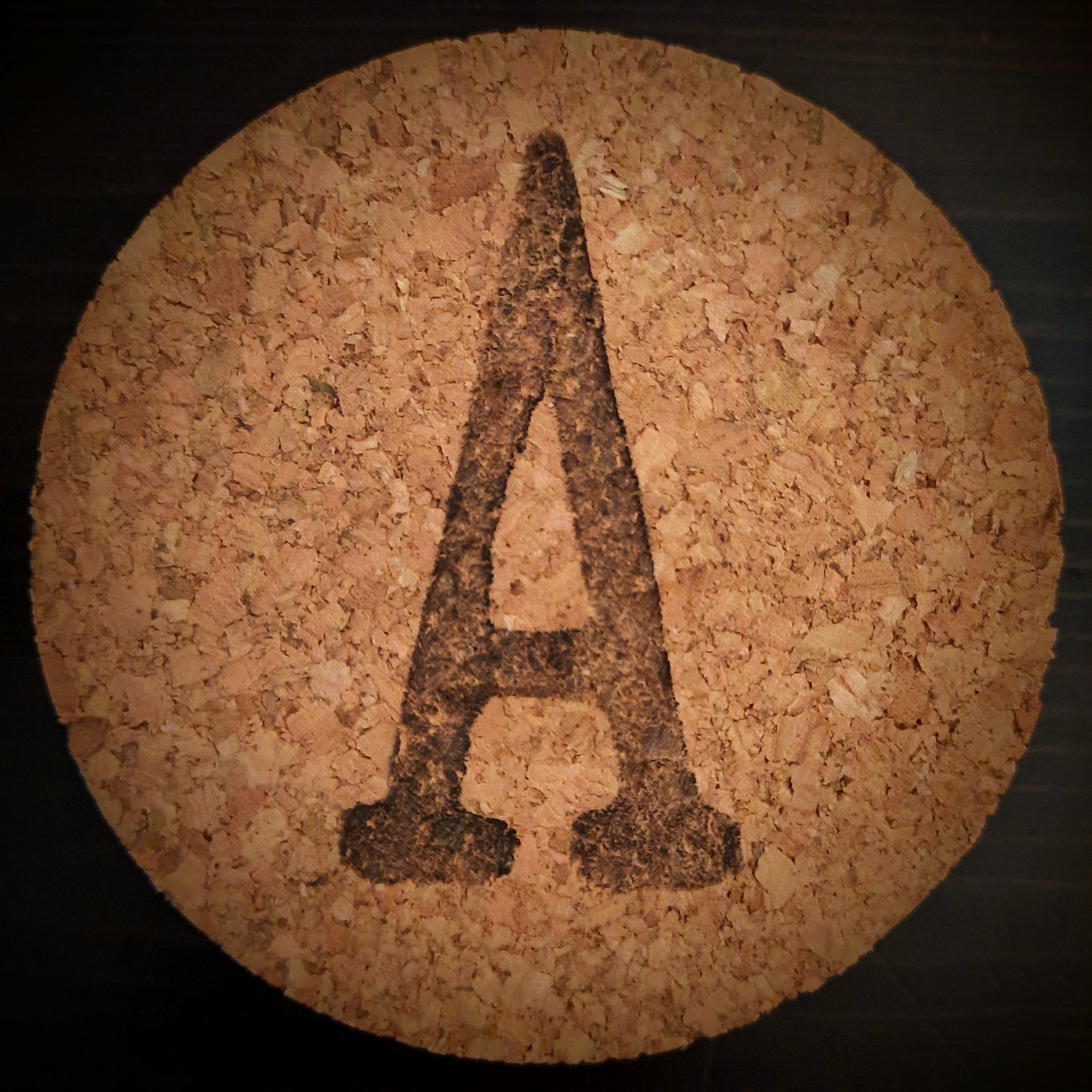 a round cork lid on black background with capital letter A stamped in black