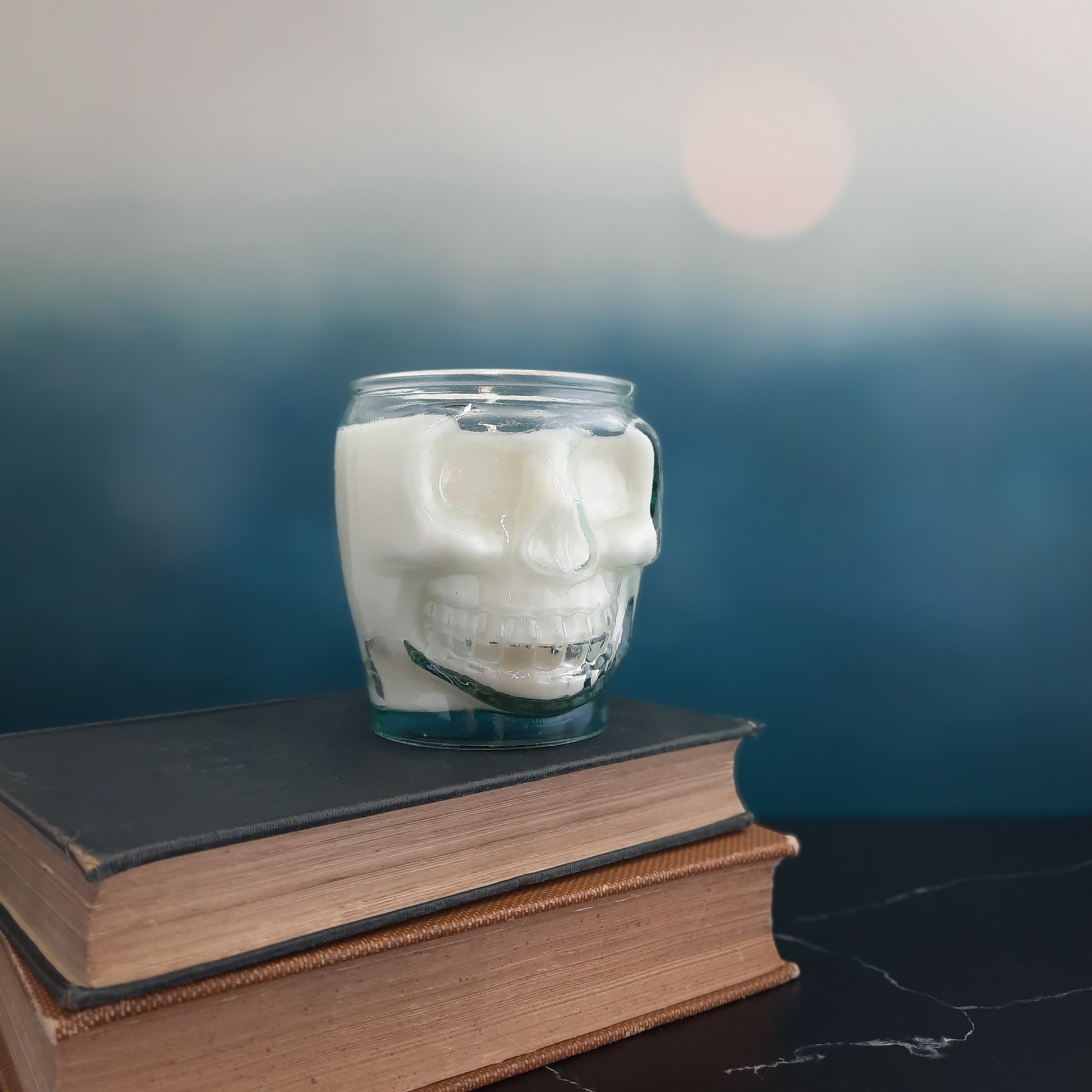 white skull candle on stack of books with blue backdrop