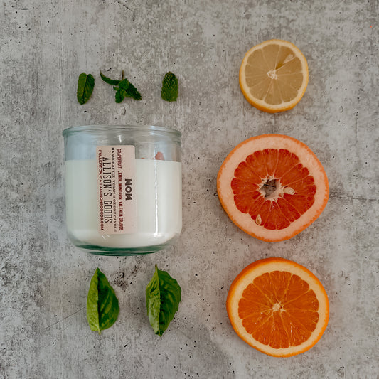 flat lay of sustainable vegan candle jar on cement with orange lemon grapefruit mint and leaves