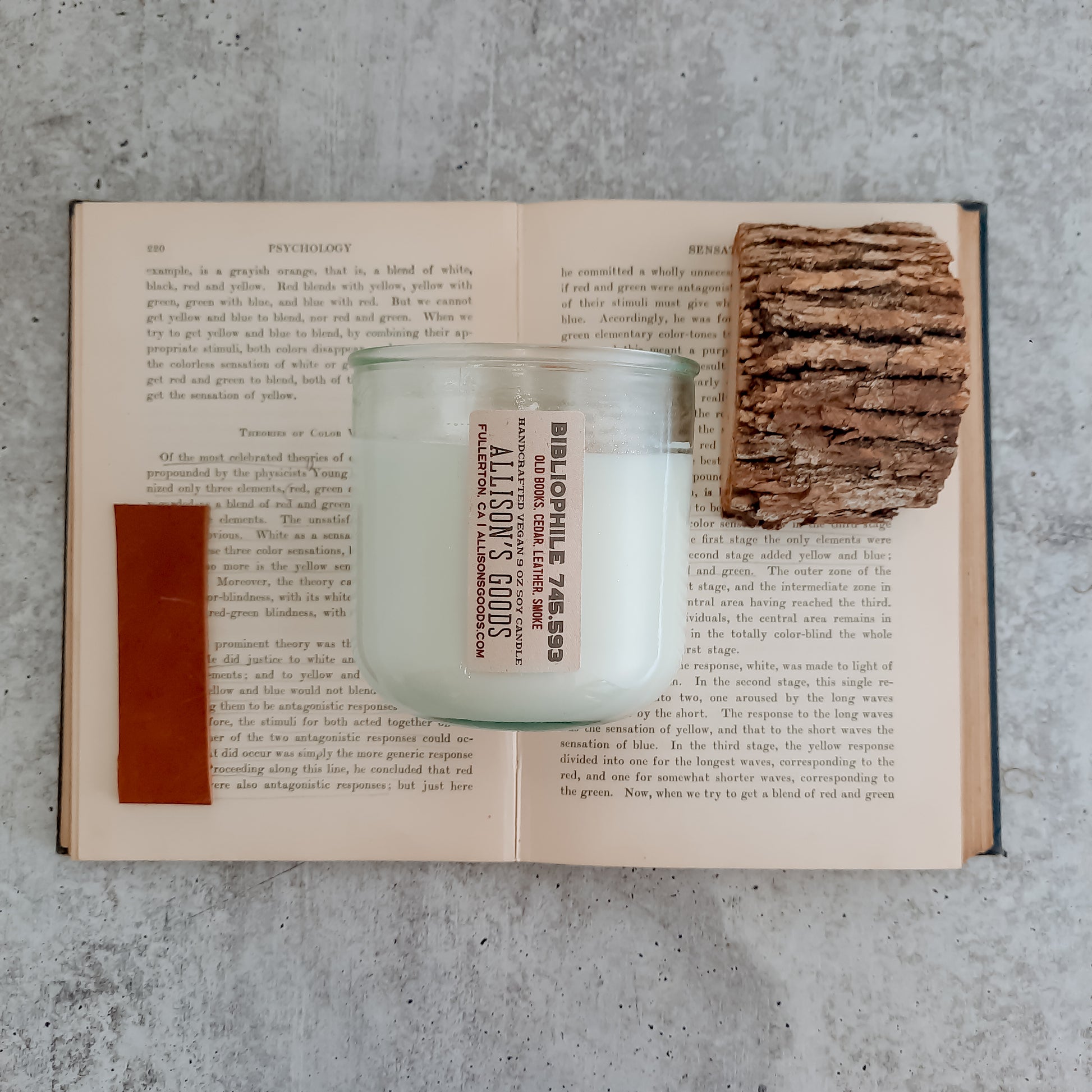 white candle jar flatlay on antique book with piece of leather and slice of wood