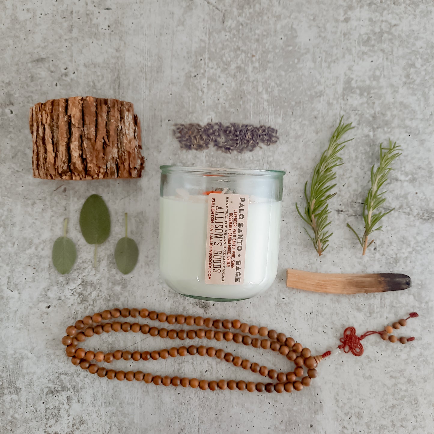 flat lay of sustainable vegan candle jar on cement with moss palo santo sage lavender and sandalwood mala beads